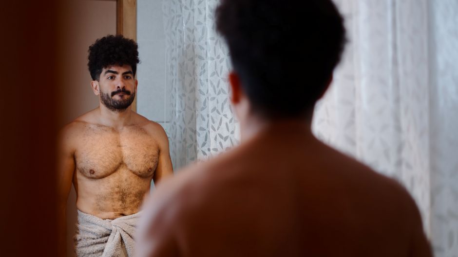 man looking in mirror with towel around waist